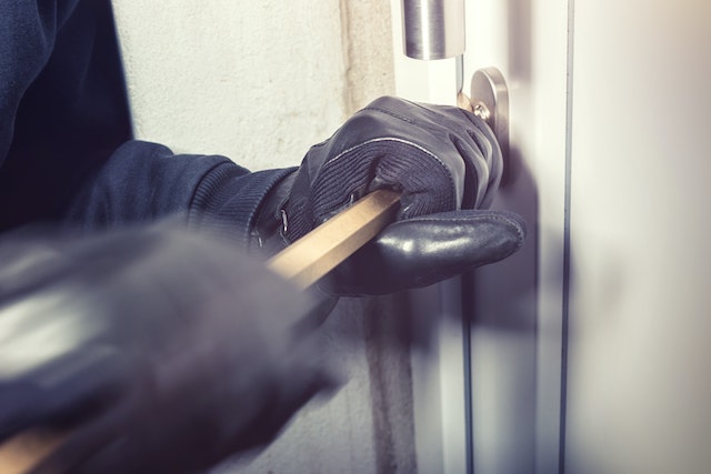 gloved hands using a crowbar to open a door